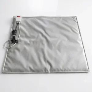 A high-angle product photograph of an IBC heating base, shown as a large, square, reflective gray quilted fabric mat. A white power controller box with a red switch is attached to one corner, with black power cables and a separate grey temperature sensor probe neatly coiled and extending from it, all isolated on a seamless white studio background.